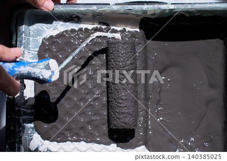Close up of paint roller loaded with dark paint inside tray. Concept of wall painting Close up of paint roller loaded with dark paint inside tray. Concept of wall painting 140385025