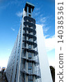 A massive outdoor spiral staircase of a high-rise apartment building stretches beautifully towards the blue sky. 140385361
