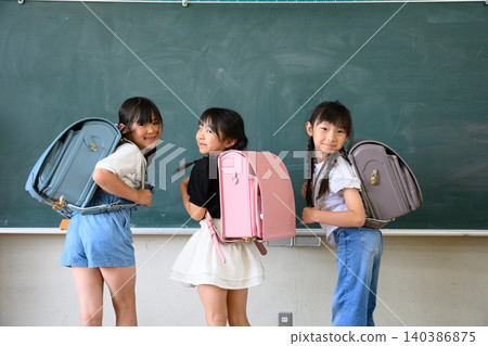 背著色彩鮮豔的書包的新女生們微笑著轉身站在教室黑板前。 背著色彩鮮豔的書包的新女生們微笑著轉身站在教室黑板前。 140386875