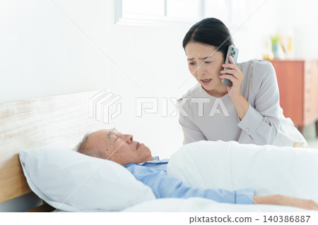 A bedridden elderly man; a woman making a phone call. A bedridden elderly man; a woman making a phone call. 140386887