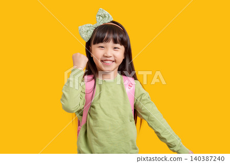 Happy Asian schoolgirl celebrating success with fist, excited child with backpack on yellow background, victory and achievement concept Happy Asian schoolgirl celebrating success with fist, excited child with backpack on yellow background, victory and achievement concept 140387240