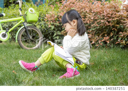Cute Asian girl reading book on green grass in park, outdoor learning and childhood education concept Cute Asian girl reading book on green grass in park, outdoor learning and childhood education concept 140387251