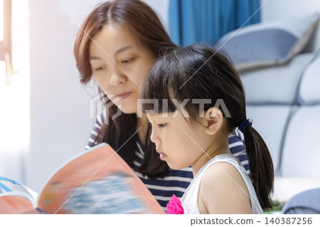 Mother reading a storybook to her young daughter at home for early education Mother reading a storybook to her young daughter at home for early education 140387256
