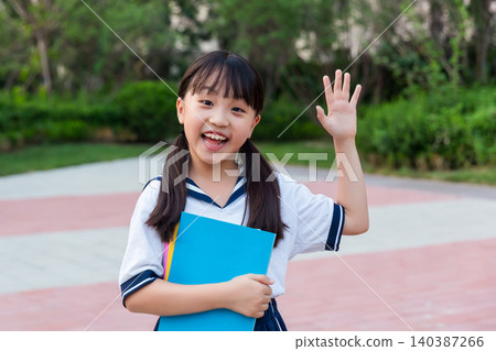 Smiling Asian schoolgirl holding books and waving, primary school education and back to school concept Smiling Asian schoolgirl holding books and waving, primary school education and back to school concept 140387266