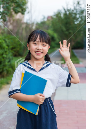 Smiling Asian schoolgirl holding books and waving, primary school education and back to school concept 140387267