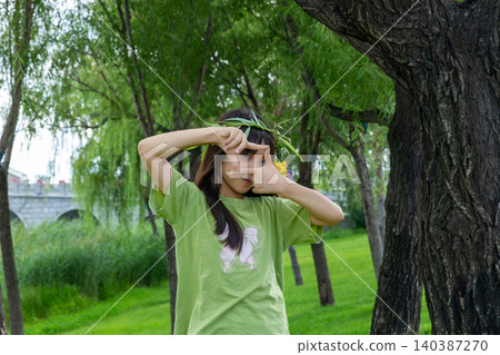 A creative young girl making a camera frame gesture with her hands over her face in the woods. A creative young girl making a camera frame gesture with her hands over her face in the woods. 140387270