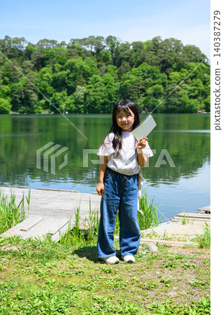 一群小學生在湖邊郊遊,她們興高采烈地舉起手,手裡拿著書籤,周圍是綠樹成蔭的湖面。 一群小學生在湖邊郊遊,她們興高采烈地舉起手,手裡拿著書籤,周圍是綠樹成蔭的湖面。 140387279