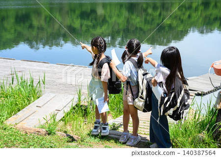 一群小學生女孩手拿地圖,站在湖邊綠樹環繞的環境中,抬頭望向遠方,臉上帶著驚訝的表情。 一群小學生女孩手拿地圖,站在湖邊綠樹環繞的環境中,抬頭望向遠方,臉上帶著驚訝的表情。 140387564
