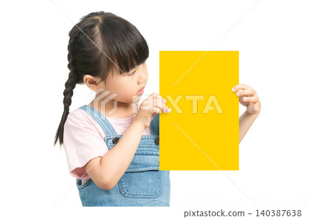 Asian Little Girl with Braided Hair Looking at Yellow Paper Card on White Background Asian Little Girl with Braided Hair Looking at Yellow Paper Card on White Background 140387638