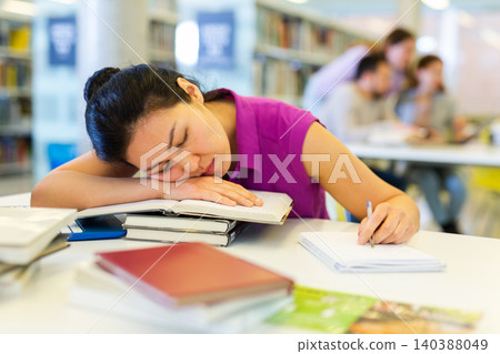 Tired woman lying on books at library 140388049