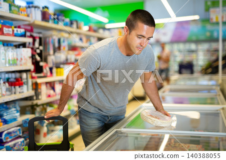 Man choosing frozen pizza dough in refrigerated display case in supermarket 140388055