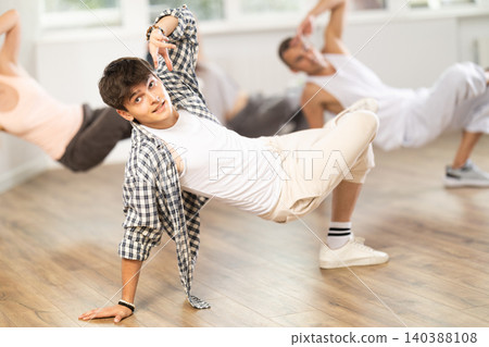 Man and his students perform hip hop dance on one bent leg, movement in horizontal plane near floor Man and his students perform hip hop dance on one bent leg, movement in horizontal plane near floor 140388108