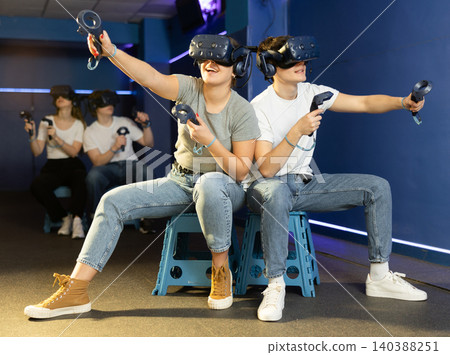 friends in helmets and with joysticks are sitting playing 3d action game. entertainment club friends in helmets and with joysticks are sitting playing 3d action game. entertainment club 140388251