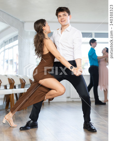 Couple in evening dresses enjoys pair dance tango, interacting with each other on floor Couple in evening dresses enjoys pair dance tango, interacting with each other on floor 140388323