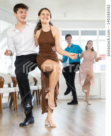 Couple in evening dresses enjoys pair dance boogie-woogie, interacting with each other on floor 140388382