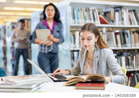 Female student studying in university library with books and laptop 140388389