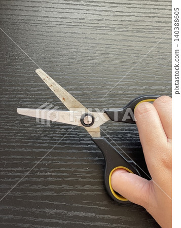 Hand Holding Rusted Scissors On Dark Wood Table Hand Holding Rusted Scissors On Dark Wood Table 140388605