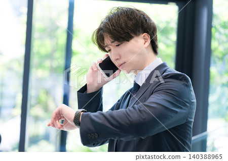 A busy businessman checking the time on his watch while on a phone call – an image of being in a hurry and being late. A busy businessman checking the time on his watch while on a phone call – an image of being in a hurry and being late. 140388965