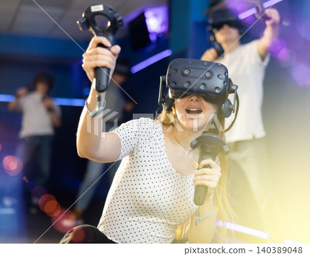 Young woman in virtual glasses plays virtual reality games with friends in special room Young woman in virtual glasses plays virtual reality games with friends in special room 140389048