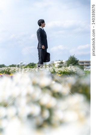 A man in a suit gazes into the distance in a flower field bathed in spiritual light. 140389076