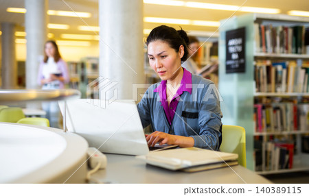 Portrait of positive woman with laptop in public library Portrait of positive woman with laptop in public library 140389115
