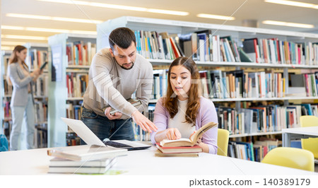Male and female students preparing for exam together in library Male and female students preparing for exam together in library 140389179