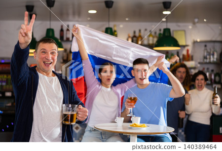 Happy friends of different ages drinking beer and celebrating the victory of the Russian team in night bar 140389464
