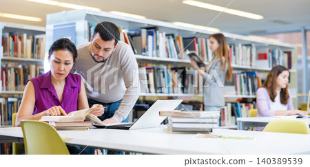 Students in the library are studying on a laptop and looking for information in books Students in the library are studying on a laptop and looking for information in books 140389539