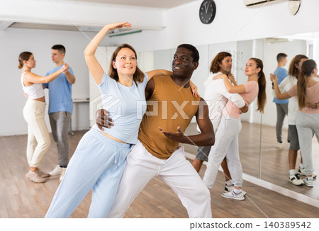 Smiling young adult couples dancing together in pairs and practicing new movements in modern studio 140389542