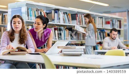 Caring woman helping friend to prepare for exams in library Caring woman helping friend to prepare for exams in library 140389559