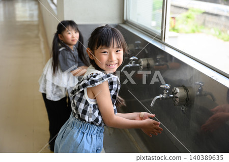 小學生在學校的飲水機前快樂地洗手。 小學生在學校的飲水機前快樂地洗手。 140389635