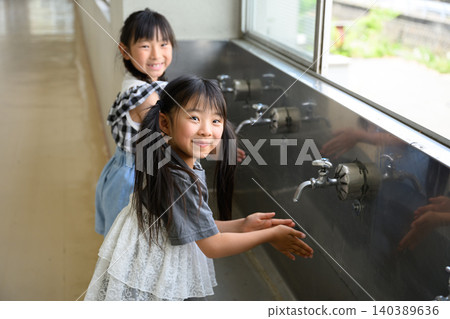 Elementary school girls happily washing their hands at the school's water fountain. Elementary school girls happily washing their hands at the school's water fountain. 140389636
