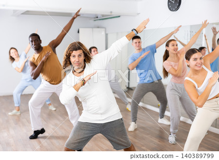 Group of sporty young adult multinational sports people making straight line with hands exercising dancing in gym Group of sporty young adult multinational sports people making straight line with hands exercising dancing in gym 140389799