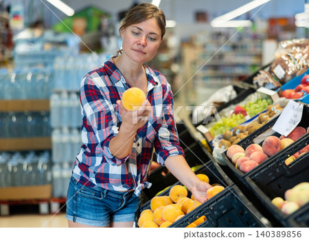 Portrait of young female choosing fresh peaches on supermarket Portrait of young female choosing fresh peaches on supermarket 140389856
