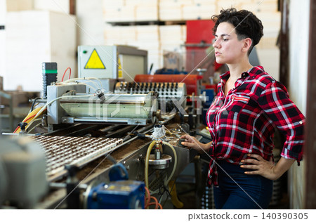 Confident woman machine operator working with automatic conveyor filling and seeding of plants in greenhouse 140390305