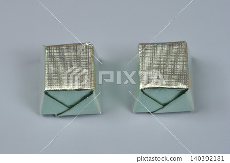 Two cube shaped chocolates wrapped in silver foil on grey background 140392181
