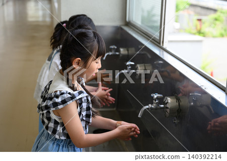 Elementary school girls carefully washing their hands at the school's water fountain. Elementary school girls carefully washing their hands at the school's water fountain. 140392214