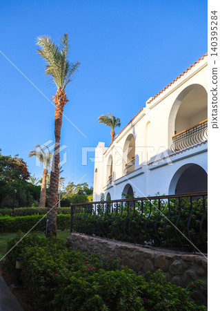 Classic resort in an Arab country with white buildings, palm trees, and serene coastal architecture under clear blue sky 140395284