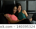 Happy young woman in green cloth that hug her smiling couple while lying on bed and using tablet pc together at home relaxing on weekend morning 140395324