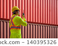 Asian man worker talking on walkie talkie for control loading containers box while standing in front of red containers at cargo shipping yard 140395326
