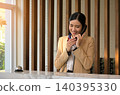Smiling Asian female hotel receptionist in yellow blazer talking on landline telephone at luxury hotel front desk with service bell 140395330