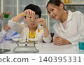 Asian female teacher guiding young student in science experiment with test tubes in school laboratory 140395331