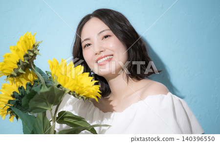 A smiling woman holding a bouquet of sunflowers against a light blue background, evoking a refreshing image of midsummer. A smiling woman holding a bouquet of sunflowers against a light blue background, evoking a refreshing image of midsummer. 140396550