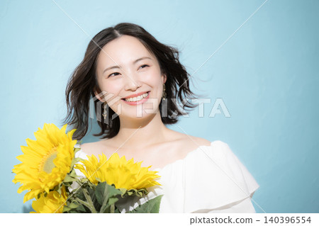 A smiling woman holding a bouquet of sunflowers against a light blue background, evoking a refreshing image of midsummer. A smiling woman holding a bouquet of sunflowers against a light blue background, evoking a refreshing image of midsummer. 140396554