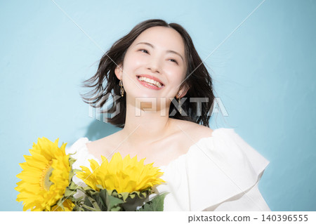 A smiling woman holding a bouquet of sunflowers against a light blue background, evoking a refreshing image of midsummer. A smiling woman holding a bouquet of sunflowers against a light blue background, evoking a refreshing image of midsummer. 140396555