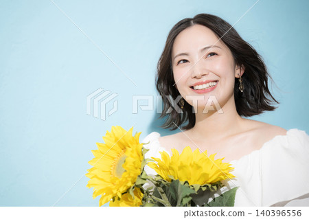 A smiling woman holding a bouquet of sunflowers against a light blue background, evoking a refreshing image of midsummer. 140396556