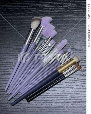 Flat Lay of Makeup Brushes with Purple Handles on Dark Surface 140396631