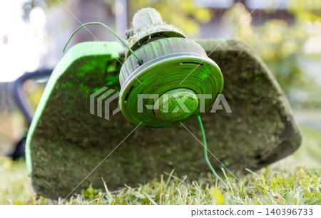 String trimmer head close up on green grass lawn. Ground level portrait of grass cutter machine with nylon line, garden weed eater tool, lawn mowing and backyard maintenance concept 140396733