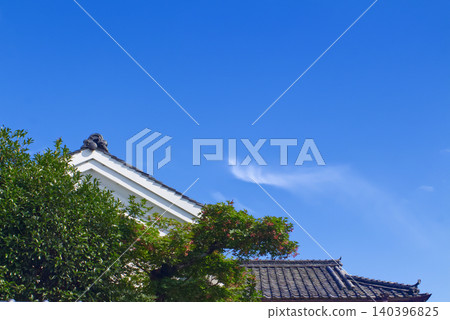 A traditional Japanese house with a tiled roof and lush greenery stands out against the early summer blue sky on Shinmachi Street in Gojo City, Nara Prefecture (a scene of traditional architecture). A traditional Japanese house with a tiled roof and lush greenery stands out against the early summer blue sky on Shinmachi Street in Gojo City, Nara Prefecture (a scene of traditional architecture). 140396825