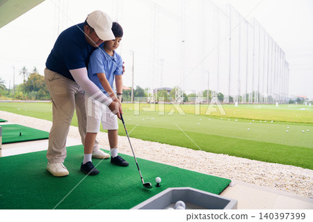 Golf instructor teaching young student proper swing at driving range Golf instructor teaching young student proper swing at driving range 140397399